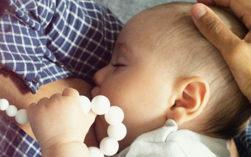 bébé qui tête et qui tient un collier d'allaitement dans ses mains